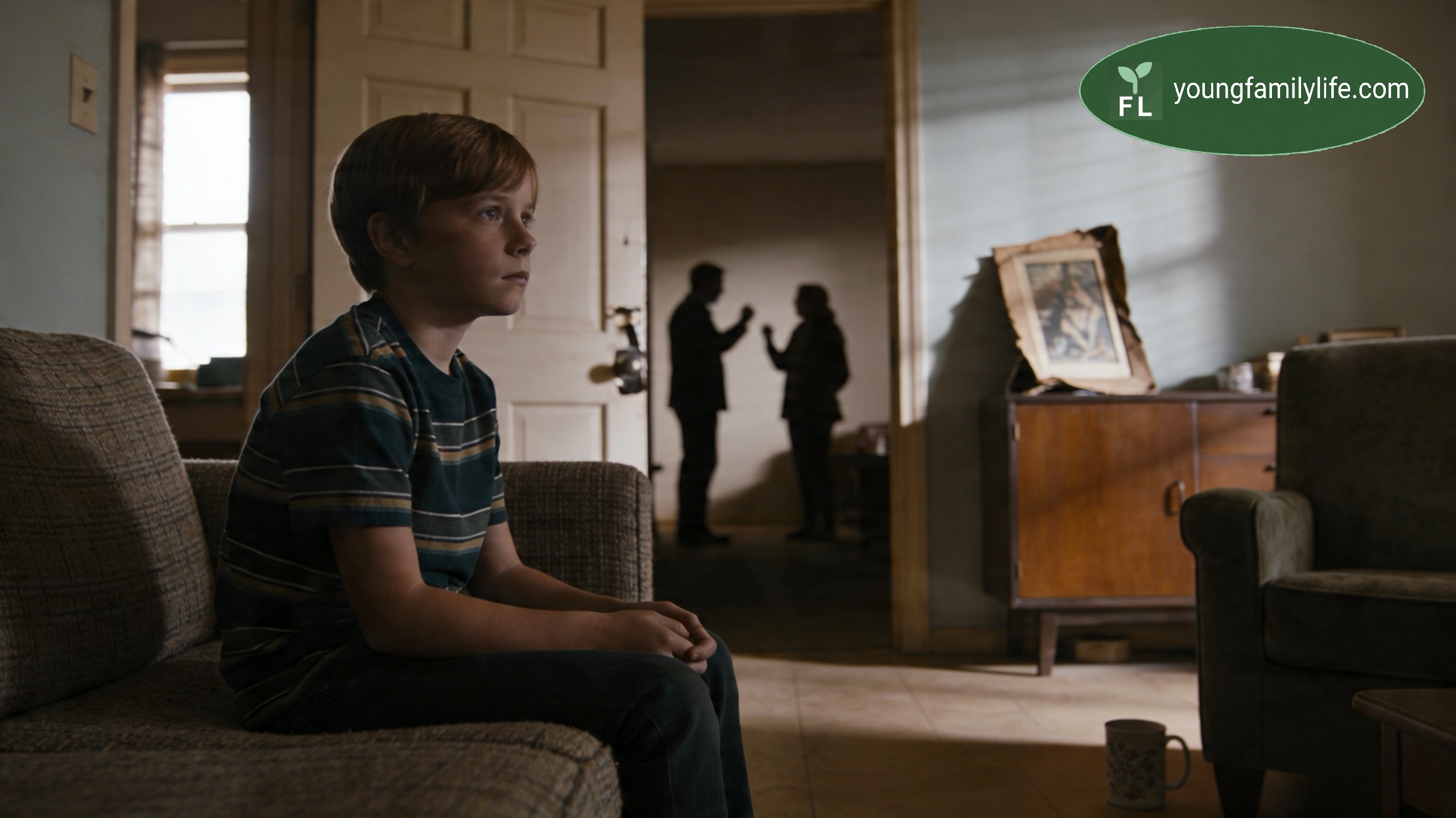 A child sitting quietly indoors, looking toward a window, in a contemplative pose.