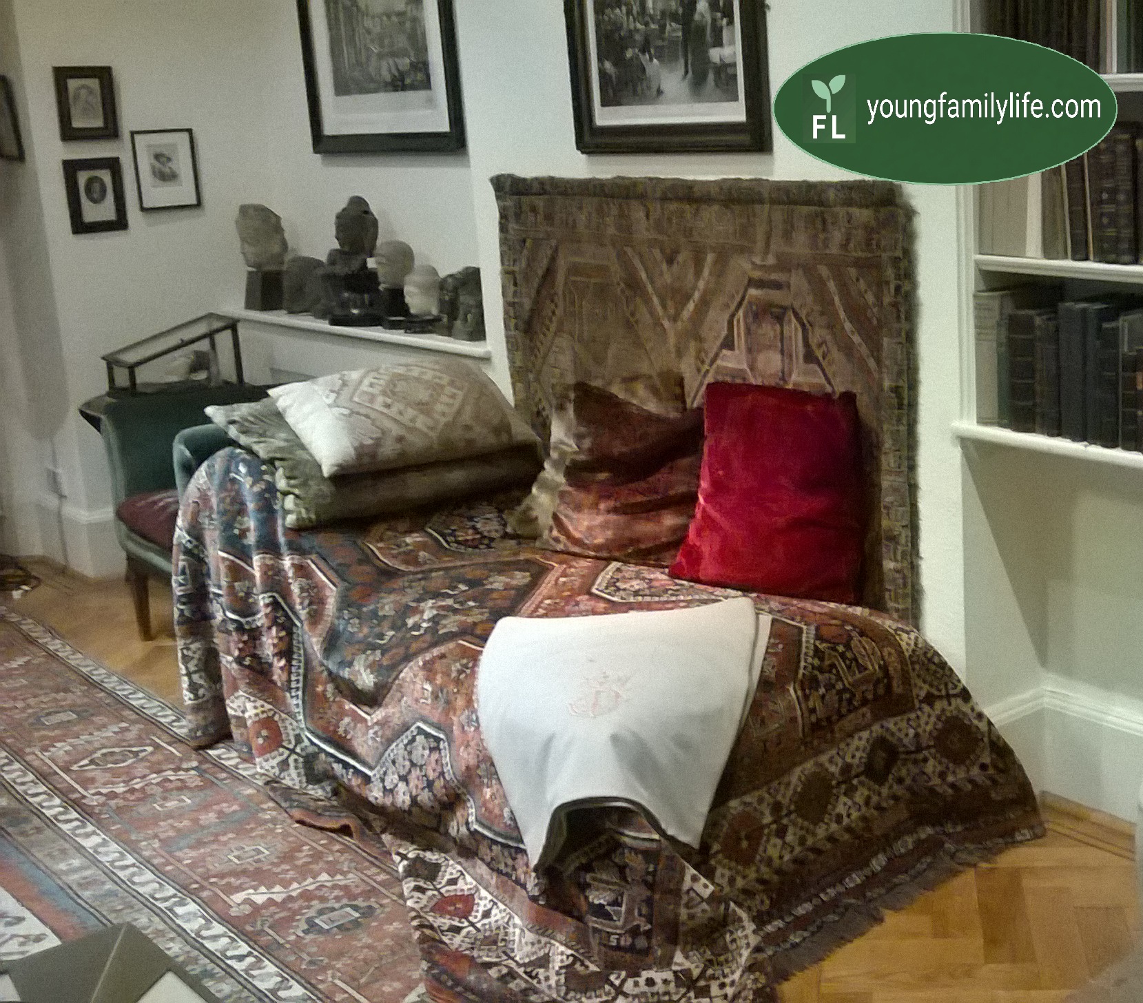Freud's famous couch draped in a Persian rug and cushions, with a white sculptural figure of a seated woman positioned beside it. Behind, floor-to-ceiling bookshelves packed with dark-bound volumes. Photographed at the Freud Museum, London, October 2016.